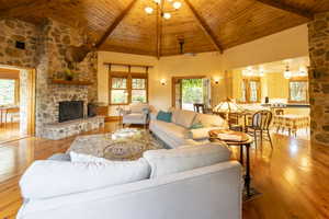 Living area featuring a stone fireplace with a wood mantle, wood-finish flooring, and a vaulted wood-paneled ceiling