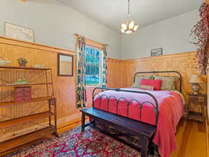 Bedroom featuring wooden walls, wood finished floors, a wainscoted wall, and a chandelier