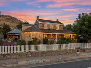 View of front of house featuring covered porch, stone siding, a fenced front yard, and a chimney