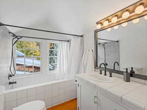 Bathroom featuring vanity, shower / bathtub combination with curtain, and lofted ceiling