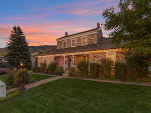 View of front of property featuring stone siding, a porch, a yard, and a chimney