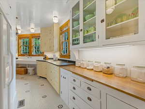 Kitchen with wood counters, white refrigerator with ice dispenser, and cream cabinetry