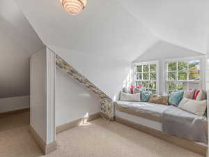Bedroom with vaulted ceiling, light colored carpet, and wallpapered walls