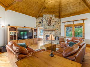 Living room with light wood finished floors, high vaulted ceiling, a wood ceiling with exposed beams, and a stone fireplace