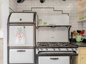 Kitchen with dark countertops, black range with gas stovetop, open shelves, and backsplash
