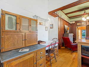 Kitchen featuring wood walls, light wood-style floors, brown cabinetry, glass insert cabinets, and dark countertops