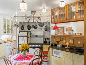 Kitchen featuring glass insert cabinets, decorative backsplash, hanging light fixtures, and gas stove