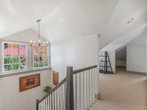 Hall with an upstairs landing, lofted ceiling, a chandelier, and light colored carpet