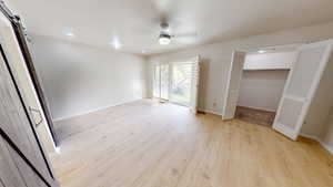 Unfurnished bedroom featuring a barn door, light wood-style floors, a walk in closet, ceiling fan, and access to outside