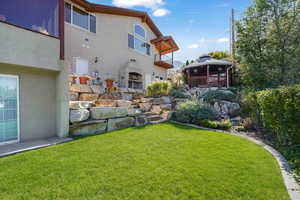 Rear view of house featuring stucco siding, a lawn, stone siding, a balcony, and a fireplace