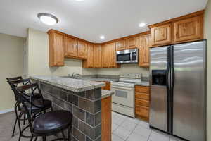 Second Kitchen featuring stainless steel appliances, knotty alder cabinetry, recessed lighting, a kitchen bar, light tile patterned flooring, and a peninsula