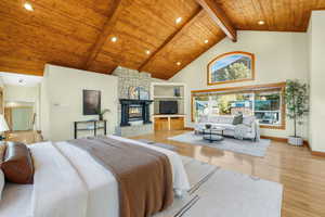 Primary Bedroom featuring high vaulted, wooden ceiling with exposed beams, light hardwood flooring, and a large fireplace.