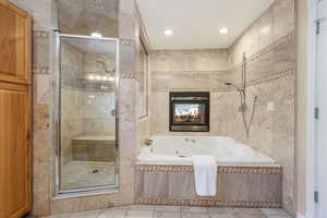 Primary en suite full bathroom with a large stall shower, oversized jetted tub, double sided fireplace, tile walls, tile patterned floors, and recessed lighting