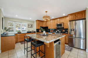 Kitchen featuring stainless steel appliances, granite countertops and backsplash, knotty alder cabinets, Travertine tile flooring, and a breakfast bar area