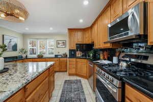 Kitchen featuring stainless steel appliances, knotty alder cabinets, granite countertops and backsplash, crown molding, and recessed lighting