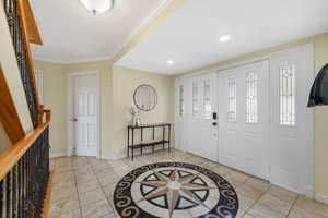 Foyer entrance featuring inlaid floor details, crown molding, light tile patterned floors, recessed lighting, and stairway