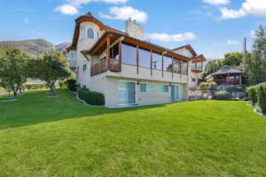 Rear view of house featuring stucco siding, a yard, a chimney, and a balcony