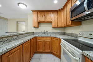 Second Kitchen with electric stove, stainless steel microwave, light stone countertops, knotty alder cabinetry, and a textured ceiling