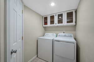 Laundry area featuring washing machine and dryer, light tile patterned flooring, and cabinet space