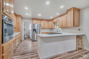 Kitchen with light countertops, a peninsula, recessed lighting, stainless steel appliances, and light brown cabinetry
