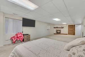 Bedroom with carpet flooring, a drop ceiling, and a fireplace with raised hearth