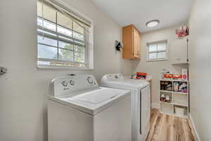 Laundry area with light wood-style floors, washer and dryer, and cabinet space