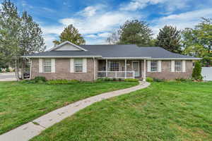 Ranch-style house with a front yard, covered porch, brick siding, and a shingled roof