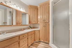 Bathroom featuring a shower stall, double vanity, and light wood-style floors
