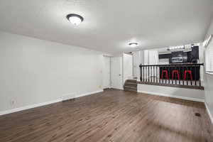 Unfurnished living room with a textured ceiling, dark wood finished floors, and stairway