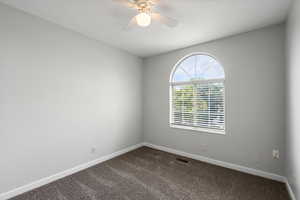 Empty room with dark colored carpet, ceiling fan, and a textured ceiling