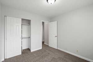 Unfurnished bedroom with dark carpet, a closet, and a textured ceiling