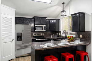 Kitchen with dark countertops, stainless steel appliances, dark cabinetry, lofted ceiling, and a breakfast bar area