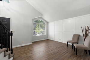 Unfurnished room with vaulted ceiling, dark wood-type flooring, stairway, and a decorative wall