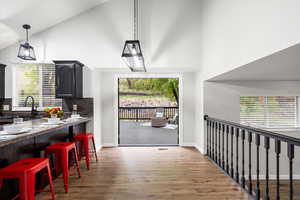 Kitchen with high vaulted ceiling, a kitchen breakfast bar, plenty of natural light, light wood finished floors, and decorative backsplash