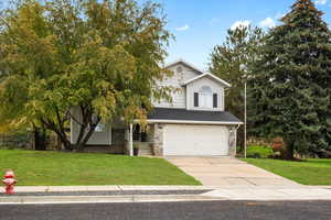 View of front facade featuring a front lawn, a garage, concrete driveway, and stone siding