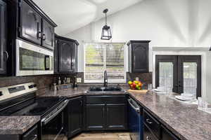 Kitchen with stainless steel appliances, healthy amount of natural light, dark cabinets, and vaulted ceiling