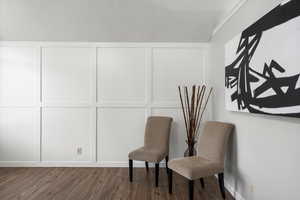 Sitting room featuring a decorative wall and dark wood-style flooring