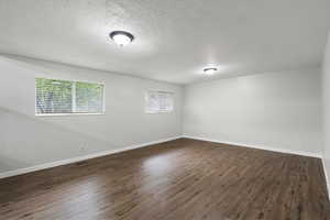 Empty room with dark wood-type flooring and a textured ceiling