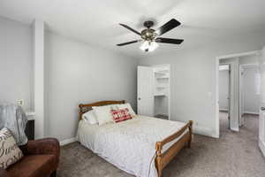 Carpeted bedroom featuring ceiling fan and a walk in closet
