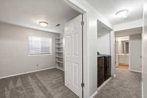 Hall featuring a textured ceiling, dark carpet, and independent washer and dryer