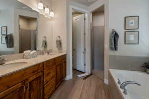 Full bath featuring a bath, double vanity, a stall shower, and light wood-type flooring