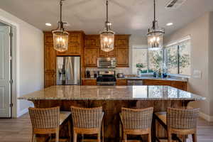 Kitchen featuring brown cabinets, wood finish floors, light stone countertops, stainless steel appliances, and a chandelier