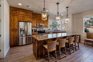 Kitchen with brown cabinetry, light stone counters, appliances with stainless steel finishes, recessed lighting, and wood finish floors