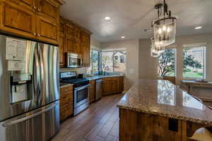 Kitchen featuring stainless steel appliances, dark stone countertops, wood finish floors, recessed lighting, and decorative light fixtures