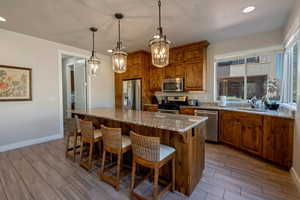 Kitchen with brown cabinetry, recessed lighting, a kitchen bar, light stone counters, and wood tiled floors
