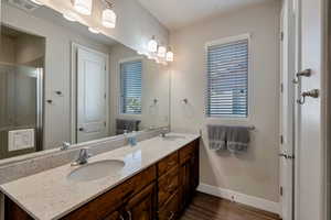 Bathroom featuring double vanity, dark wood-style flooring, and an enclosed shower