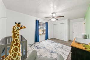 Carpeted bedroom with a closet, a textured ceiling, a ceiling fan, and a crib