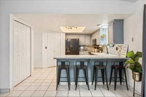 Kitchen featuring light countertops, a kitchen breakfast bar, decorative backsplash, black refrigerator with ice dispenser, and light tile patterned floors