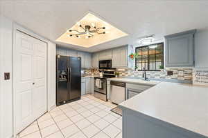 Kitchen featuring a textured ceiling, light countertops, a raised ceiling, stainless steel appliances, and gray cabinetry