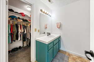 Bathroom with a textured ceiling, vanity, a spacious closet, and a textured wall